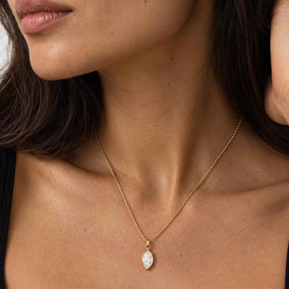 A close-up of a model wearing a delicate gold chain necklace with a teardrop-shaped pendant set with clear stones, shown against her neck and chest.